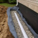 Please make a clear and realistic featured image with this Factors to Consider for Exterior French Drain Basement Waterproofingas if the image were square in size and without text